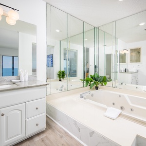 Elegant master bath featuring a jetted tub, elegant marble countertops, and stunning beach views