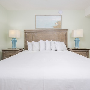 Inviting bedroom featuring a king bed with white linens, complemented by stylish blue lamps and serene coastal artwork