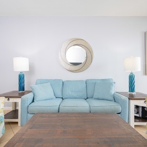 The living room features a light blue sofa, a patterned chair, and a coffee table, creating a relaxed beach vibe