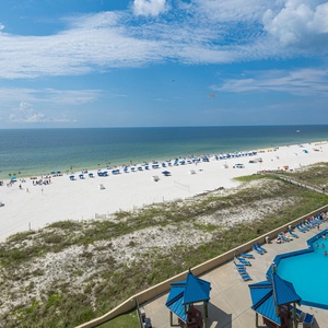Enjoy a vibrant beachfront view with white sand, colorful umbrellas, and a sparkling pool area below