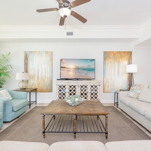Bright and airy living room featuring plush seating, a large TV, and vibrant artwork for a cozy beachside retreat