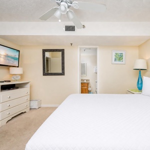 The bedroom features a king bed with white linens, a wall-mounted TV, and a bright blue lamp, creating a serene atmosphere