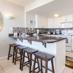 The kitchen features sleek granite countertops, plentiful appliances, and a cozy breakfast bar with four wooden stools