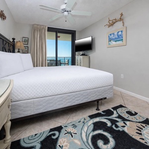 Master suite bedroom featuring a king bed, stylish decor, and a balcony view of the beach, complemented by a flat-screen TV