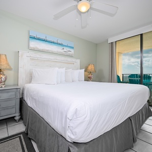 Brightly decorated master bedroom featuring a king bed, coastal artwork, and access to a balcony overlooking the beach