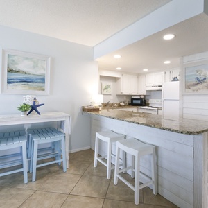 The kitchen features white cabinetry, granite countertops, and cozy breakfast bar with blue stools, perfect for casual dining