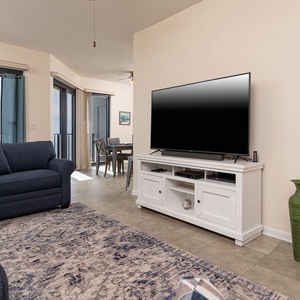 Cozy living area features a navy sofa with queen sleeper, a twin sleeping chair, large TV, and beachfront balcony view