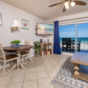 This cozy dining area features a TV, a table for meals, and a stunning view of the beachfront through sliding glass doors