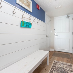 The entryway features a white bench, hooks for hanging items, and a colorful sign, creating a welcoming atmosphere