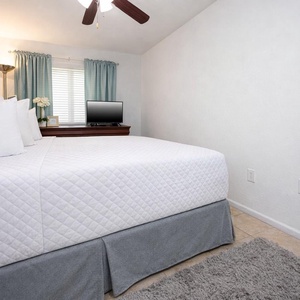 This bedroom features a comfortable bed, a TV for entertainment, and soft green curtains for a relaxing atmosphere