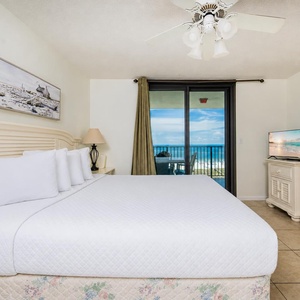 Master bedroom featuring a king bed, a TV, and a balcony with a stunning view of the beach and gulf waters