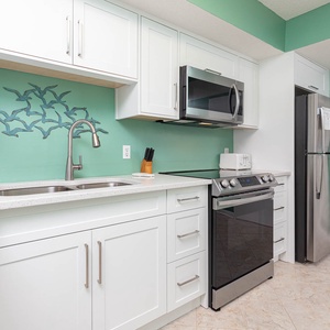 The kitchen features stainless appliances, white cabinets, and a refreshing teal accent wall for a vibrant cooking space