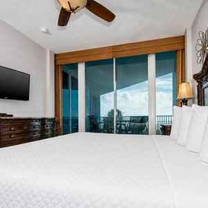 This bedroom features a plush king bed, a wall-mounted TV, and stunning beachfront views from the large glass doors