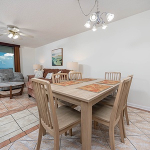 Dining area features a wooden table with six chairs, with a cozy sofa and large windows offering a beach front view