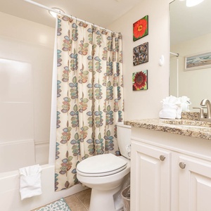 The guest bathroom features a stylish granite countertop, colorful floral decor, and a relaxing tub-shower combination