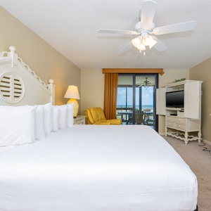 Master bedroom featuring a king bed, a cozy yellow chair, and both indoor and outdoor balcony access overlooking the gulf