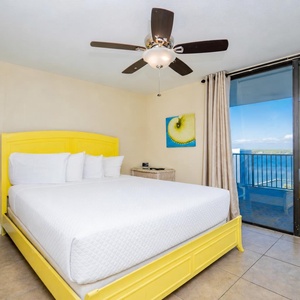 The master bedroom features a cheerful yellow king bed, a cozy nightstand, and stunning views of the water from large windows