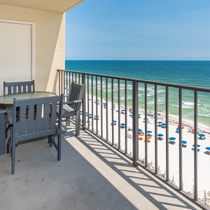 Enjoy breathtaking views from the balcony, featuring a table and chairs overlooking the serene beach and vibrant umbrellas