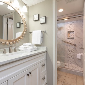 Elegant master bathroom featuring a round mirror, modern fixtures, and a walk-in shower with stylish tile accents