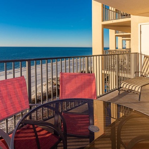 Relax on the balcony with a glass table and red chairs, overlooking the beach and tranquil blue waters