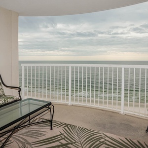 The balcony features comfortable seating with tropical-patterned cushions and offers a stunning beachfront view