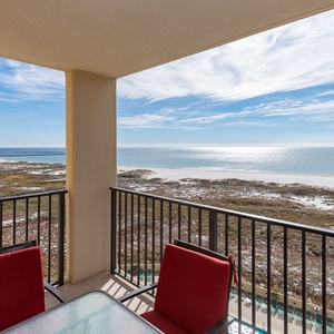 Balcony seating overlooks the tranquil beach with shimmering waters and a view of the pool area below