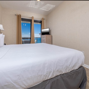 Bright master bedroom featuring a comfortable king bed, a TV, and a balcony with views of the gulf and beach