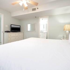 A cozy bedroom features a king bed, a TV on a light dresser, and an en-suite bathroom visible through an open door