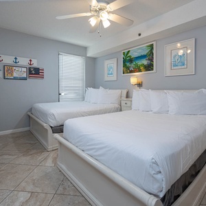 This guest bedroom features two comfortable full beds, a flat-screen TV, and vibrant coastal artwork for a relaxing stay