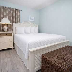 This cozy bedroom features a white bed with plush pillows, a stylish lamp, and a charming wicker storage chest