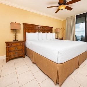 Master suite bedroom features a king bed, wooden furniture, and access to a balcony with views of the beach