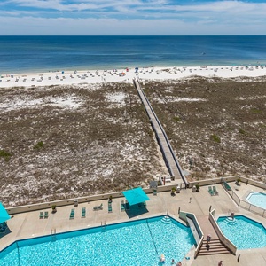 View of the pool area with turquoise umbrellas and lounge chairs, leading to the beach with its inviting white sand