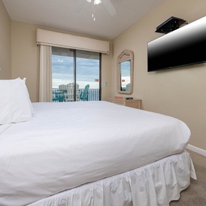 Brightly decorated master bedroom featuring a king bed, wall-mounted TV, and sliding glass doors leading to the balcony