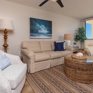 A cozy living area features a beige sofa with queen sleeper, a blue pillow, recliner, and sliding glass doors to a balcony