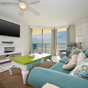 Bright living area features a teal sofa, vibrant green coffee table, and a balcony view with seating overlooking the beach