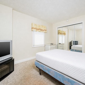 This bedroom features a comfortable bed, a TV for entertainment, and bright natural light from the window