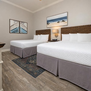 This guest bedroom features two queen beds, stylish artwork, and warm wood tones for a relaxing retreat
