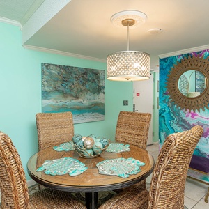 Brightly decorated dining area with woven chairs, a stylish chandelier, and vibrant artwork creating a welcoming atmosphere