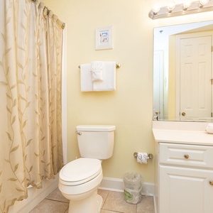 This bathroom features a bright yellow color scheme, a shower with a floral curtain, and a clean vanity with ample storage