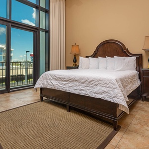 The master bedroom features a plush king bed, warm wood accents, and balcony access with beachfront views