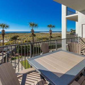 Balcony with a table and chairs offering a view of the beach, palm trees, and a clear blue sky