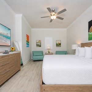 Relax in this guest bedroom featuring a king bed, vibrant artwork, and a comfortable seating nook with twin chairs