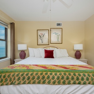 The guest bedroom features a king bed adorned with a colorful patterned throw, complemented by beach views