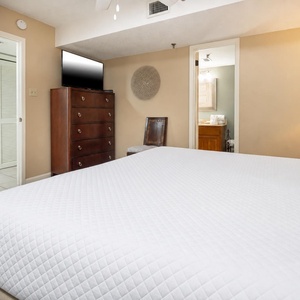 The bedroom features a king bed, a wooden dresser, a TV, and an adjoining bathroom visible through a doorway