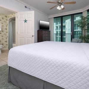 Guest bedroom featuring a plush king bed, a TV, and large windows that offer a glimpse of the balcony view