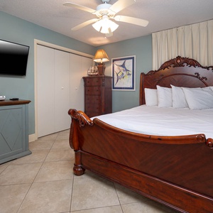 This cozy guest bedroom features elegant wood furniture with a queen bed, a flat-screen TV, and soft blue walls