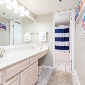 Bright master bathroom featuring a spacious vanity, decorative beach art, and a tub/shower combo with a striped curtain