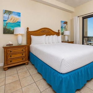 Brightly decorated master bedroom with a king bed and coastal artwork, leading to the outdoor patio