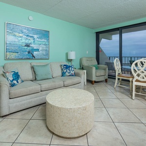 Living and dining space with coastal decor, plush seating, and expansive beach views from the large balcony windows