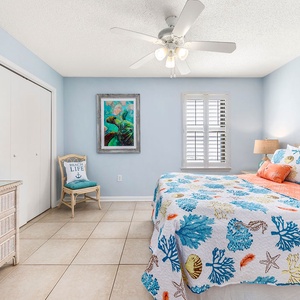 Bright guest bedroom featuring a queen bed with colorful bedding, a cozy chair, and beach artwork on the walls